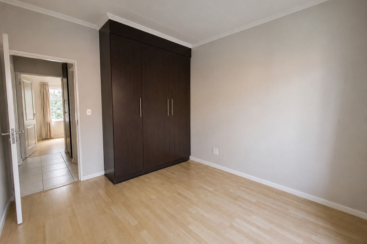 A clean, empty bedroom featuring light laminate flooring, neutral walls, and a dark wood built-in wardrobe with modern handles.