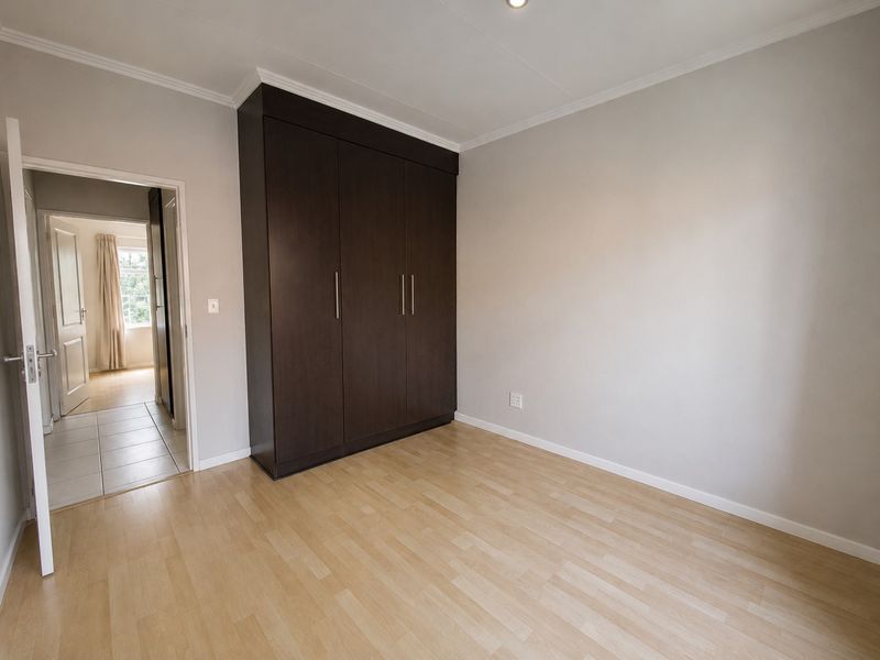 A clean, empty bedroom featuring light laminate flooring, neutral walls, and a dark wood built-in wardrobe with modern handles.