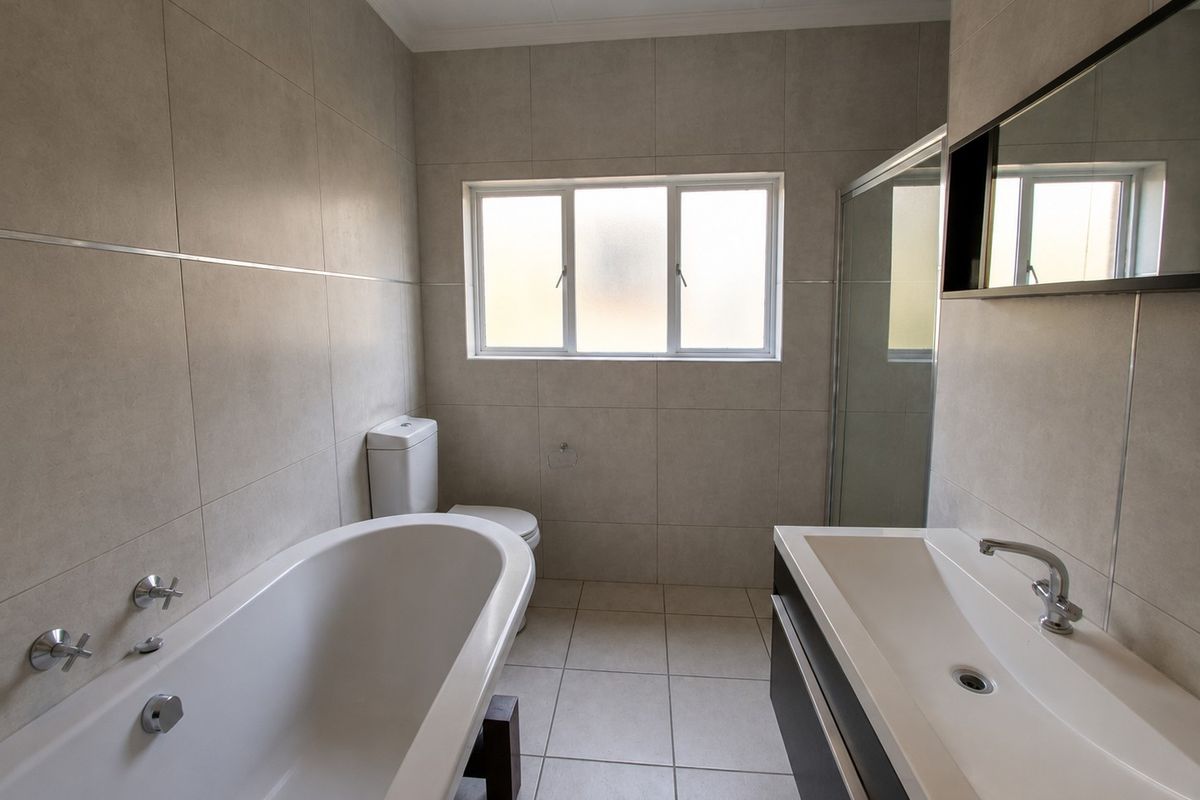 A modern, well-maintained bathroom featuring a freestanding bathtub, a sleek vanity with a basin, a separate shower enclosure, and neutral floor-to-ceiling tiling.