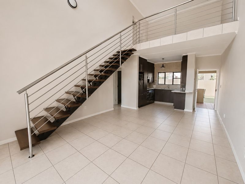 Spacious open-plan living area featuring a modern staircase with stainless steel balustrade, mezzanine level, and a functional kitchen with built-in cabinetry.