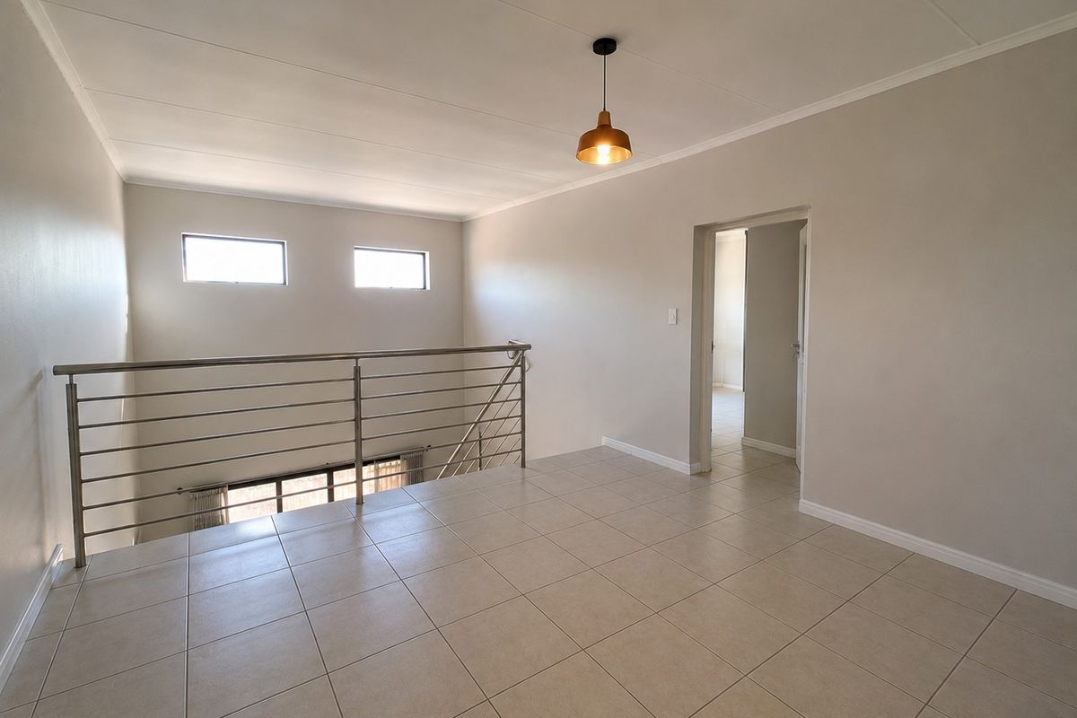 A bright, open-plan landing or living area featuring neutral tiled flooring, a modern stainless steel balustrade, and a contemporary pendant light fixture.