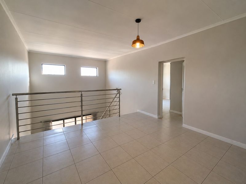 A bright, open-plan landing or living area featuring neutral tiled flooring, a modern stainless steel balustrade, and a contemporary pendant light fixture.