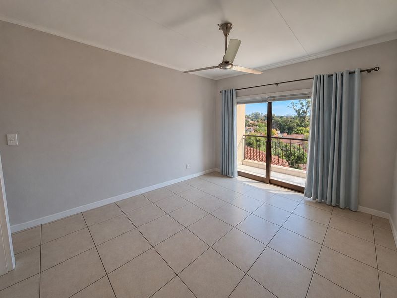 A bright, empty bedroom featuring neutral tiled flooring, a ceiling fan, and sliding glass doors that open onto a private balcony with scenic views.