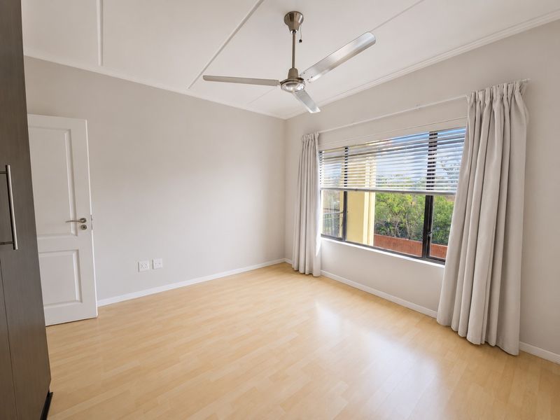 A bright, empty bedroom featuring light laminate flooring, a ceiling fan, and a built-in cupboard with neutral wall finishes.