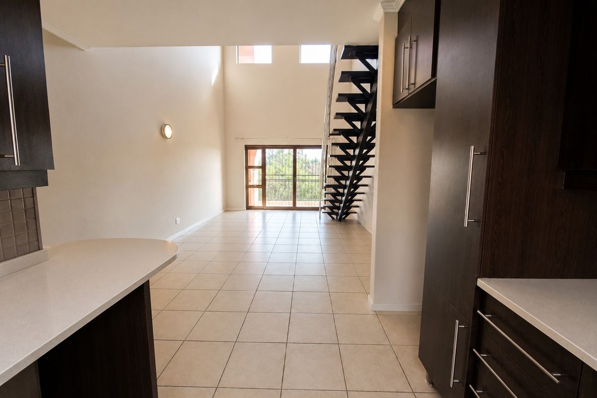 Spacious open-plan living area featuring modern dark cabinetry, stone countertops, tiled floors, and a striking metal staircase leading to an upper level.