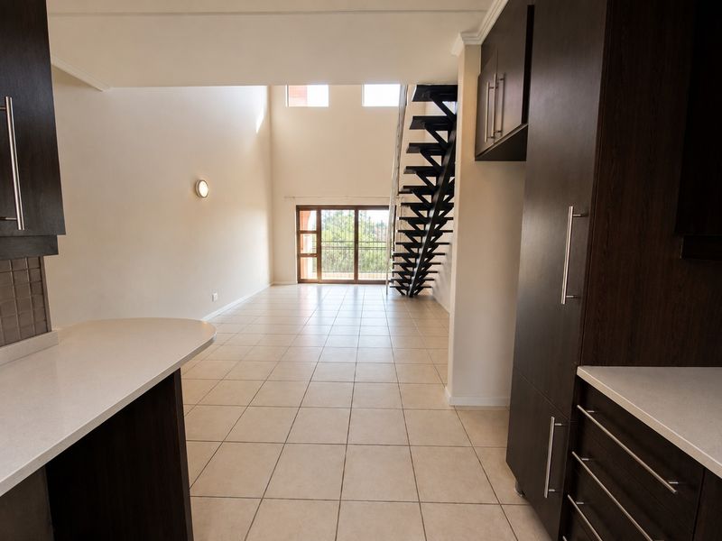 Spacious open-plan living area featuring modern dark cabinetry, stone countertops, tiled floors, and a striking metal staircase leading to an upper level.