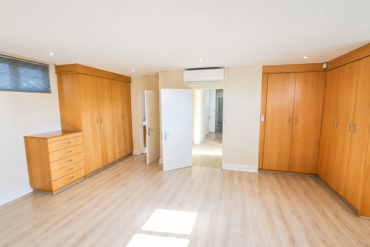 Spacious bedroom featuring extensive built-in wooden cabinetry, light laminate flooring, and a wall-mounted air conditioning unit.