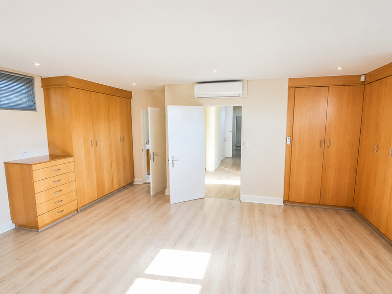 Spacious bedroom featuring extensive built-in wooden cabinetry, light laminate flooring, and a wall-mounted air conditioning unit.
