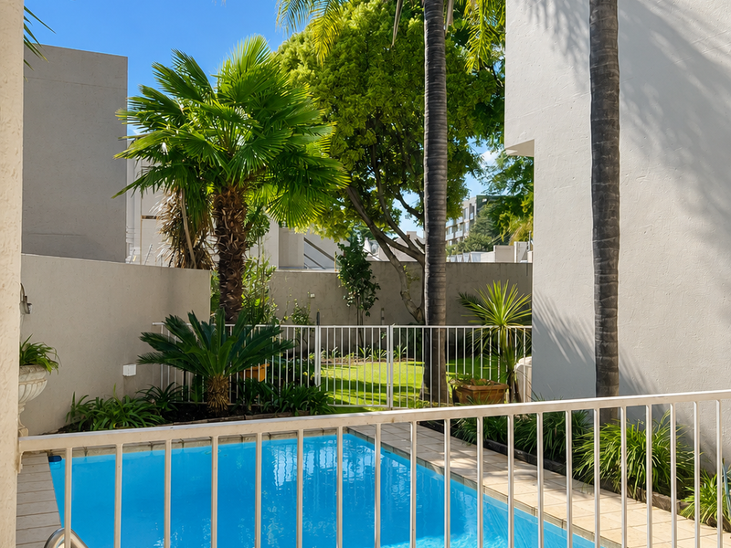 A well-maintained private swimming pool area featuring a safety fence, tiled surround, and established garden landscaping within a secure cluster property.
