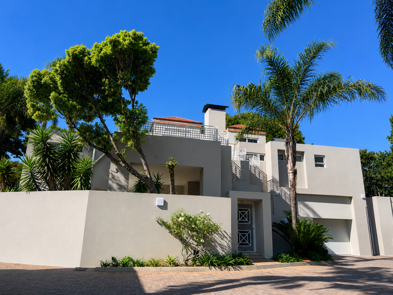 Front elevation of a modern cluster home featuring a paved driveway, integrated garage, and a secure entrance gate with established garden landscaping.