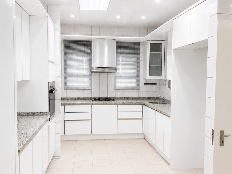 A clean, well-lit kitchen featuring white cabinetry, granite countertops, built-in oven, gas hob, and tiled flooring.