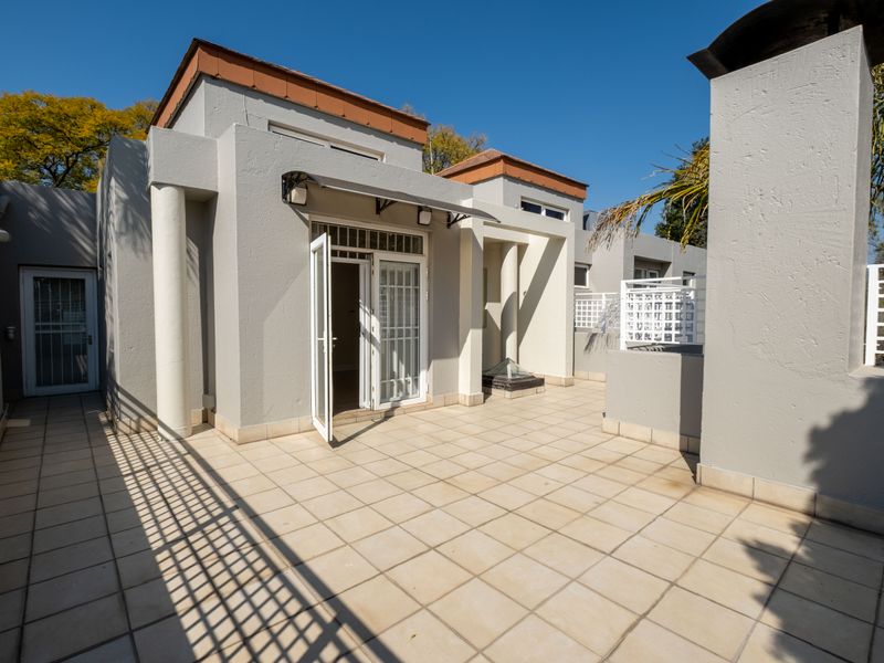 A spacious, tiled outdoor patio area featuring architectural columns, a protective awning, and direct access to the interior through double french doors.