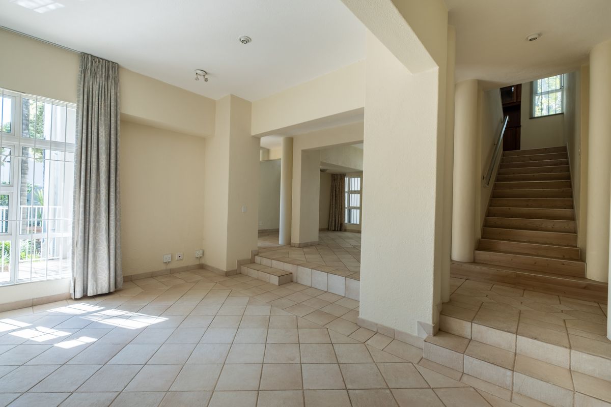 Spacious, multi-level living area featuring neutral tiled flooring, architectural columns, and a staircase leading to the upper level with ample natural light.