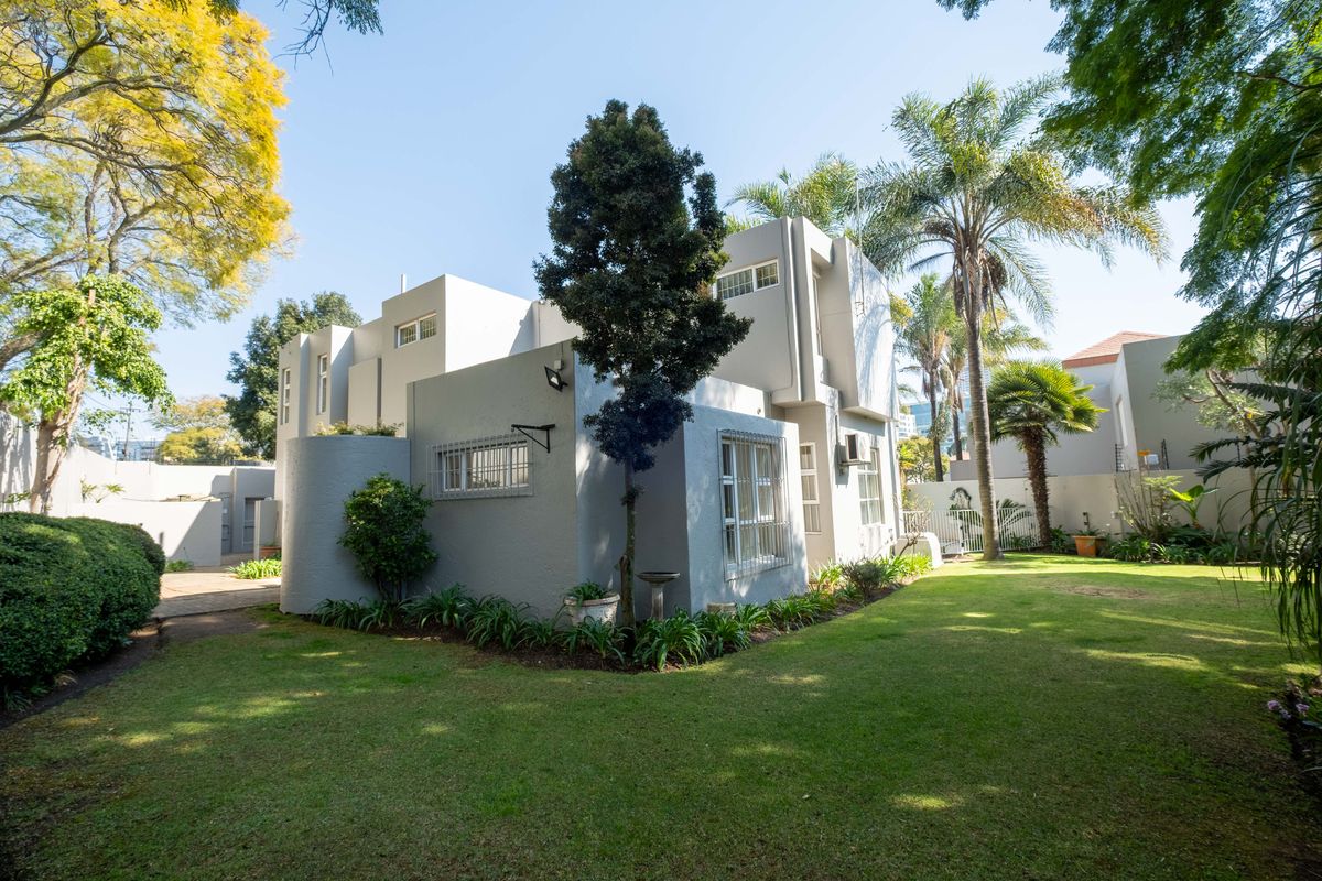 Rear view of the cluster property featuring a well-maintained garden, paved pathways, and secure window treatments.