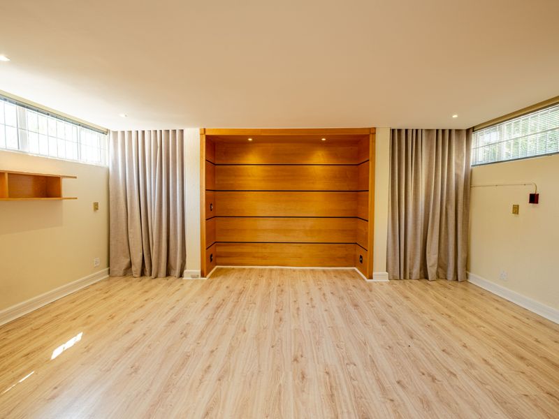 Spacious bedroom featuring light laminate flooring, high-level windows, and a prominent built-in wooden feature wall with integrated shelving and lighting.