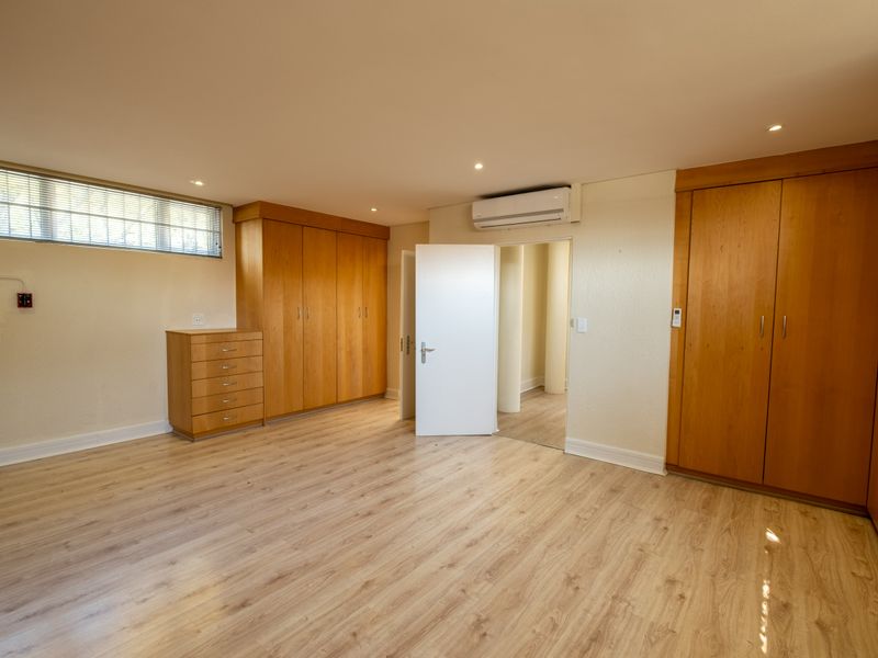 Spacious bedroom featuring light wood-look laminate flooring, extensive built-in cabinetry, and a wall-mounted air conditioning unit.