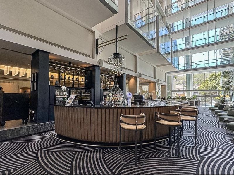 A sophisticated bar area featuring a curved counter, integrated shelving, and a striking multi-level glass atrium design in a modern penthouse setting.