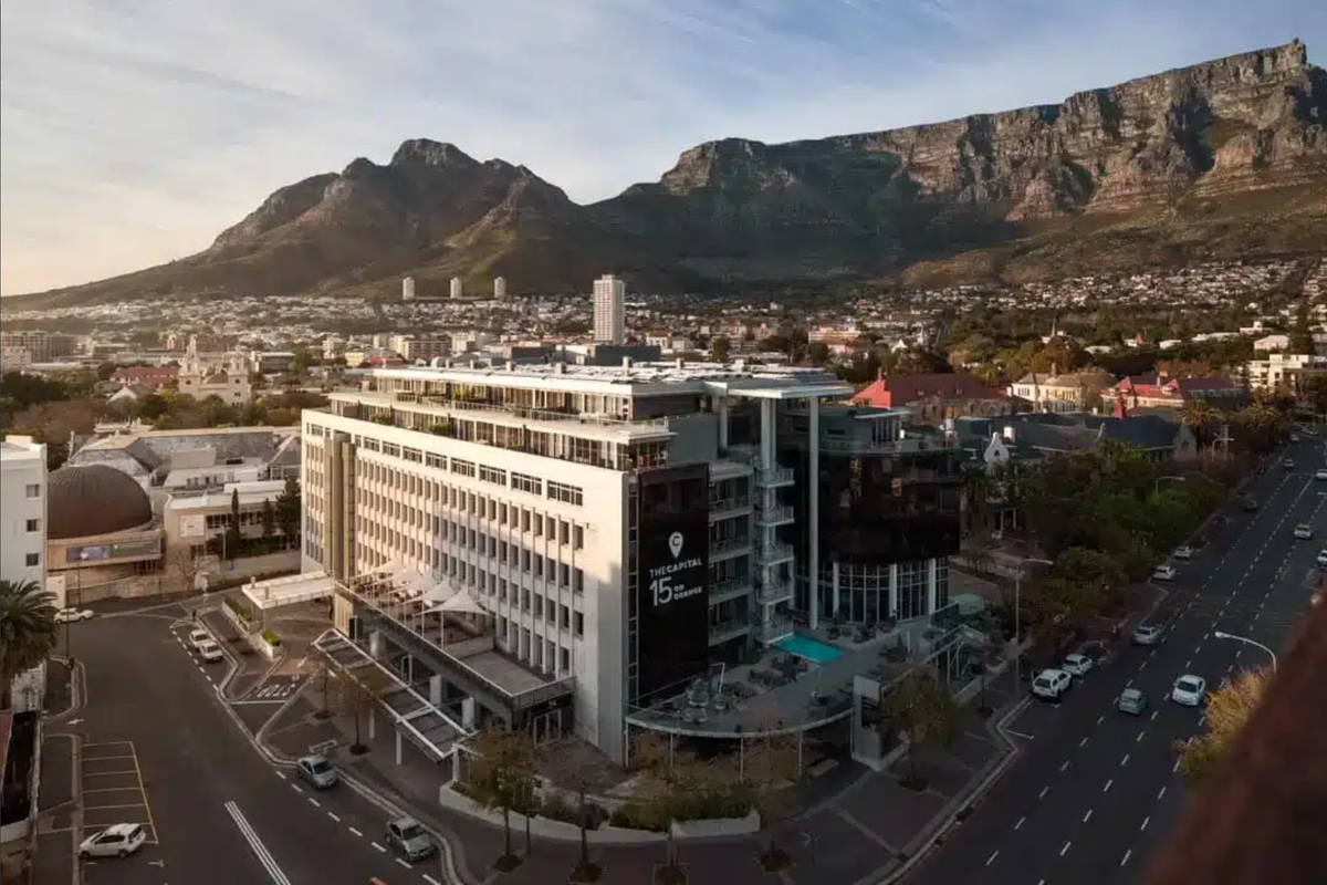 Aerial view of a modern multi-story penthouse building featuring a swimming pool, balconies, and prominent mountain views in an urban setting.