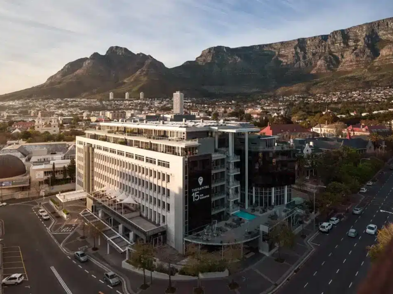 Aerial view of a modern multi-story penthouse building featuring a swimming pool, balconies, and prominent mountain views in an urban setting.