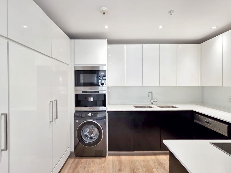 Modern kitchen featuring high-gloss cabinetry, integrated appliances including a washing machine and coffee maker, stone countertops, and a double sink.