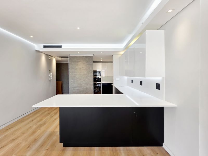 Modern open-plan kitchen area featuring sleek high-gloss cabinetry, stone countertops, integrated appliances, and recessed lighting in a contemporary penthouse setting.