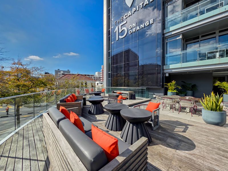 Spacious outdoor terrace featuring timber decking and a modern glass balustrade, set against the contemporary glass facade of the building.