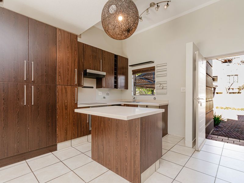 A functional kitchen featuring dark wood-look cabinetry, a central island, light countertops, and ceramic floor tiles, with direct access to an outdoor area.