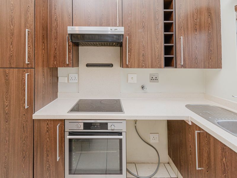 A compact kitchen featuring wood-look laminate cabinetry, stone countertops, a built-in oven, electric hob, and an integrated extractor fan.