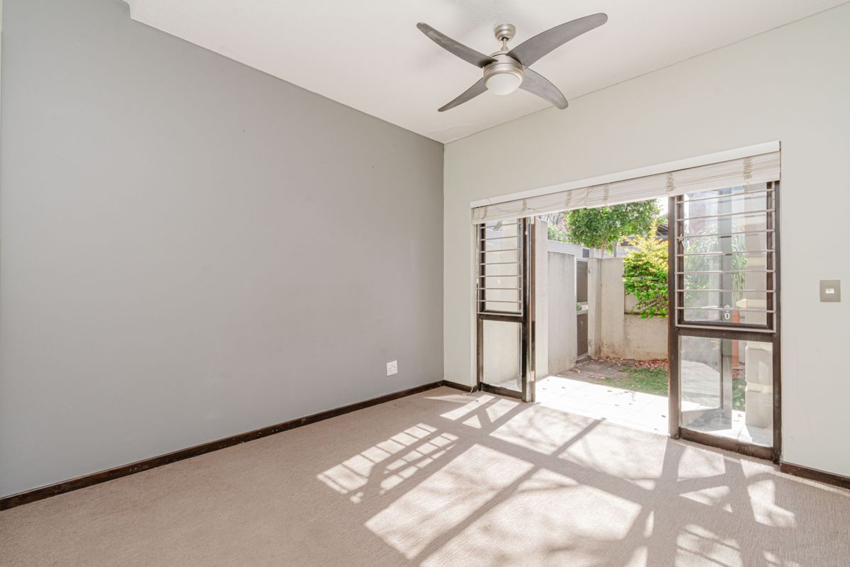 An empty bedroom featuring neutral carpet flooring, a ceiling fan, and a sliding glass door providing direct access to a private outdoor area.
