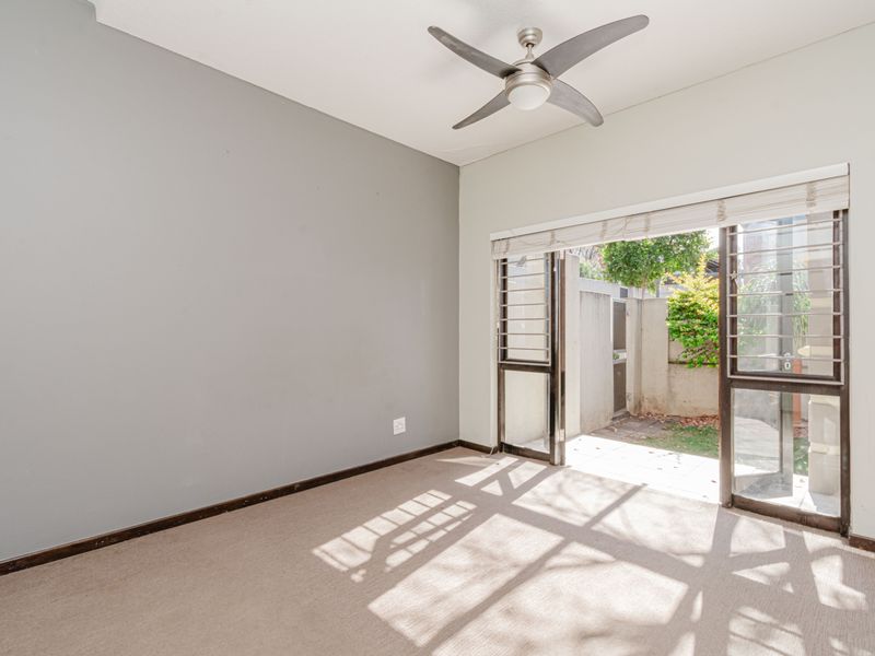 An empty bedroom featuring neutral carpet flooring, a ceiling fan, and a sliding glass door providing direct access to a private outdoor area.