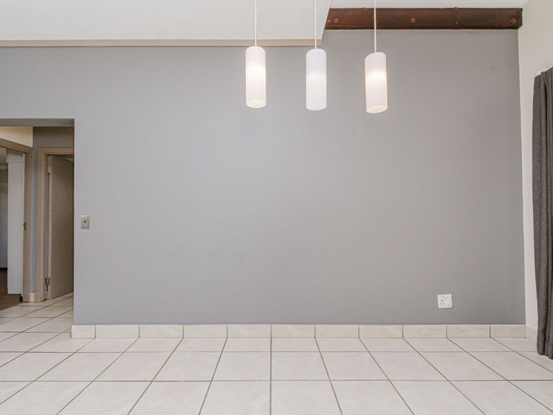 An empty living area featuring neutral grey walls, ceramic tile flooring, and modern pendant lighting with an exposed ceiling beam detail.