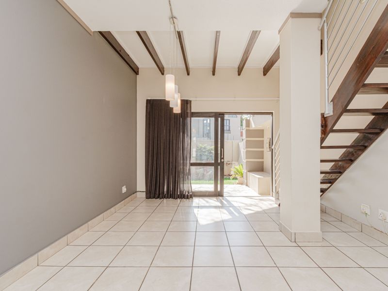 An open-plan living area featuring tiled floors, exposed timber ceiling beams, and a staircase, with direct access to an outdoor patio area.