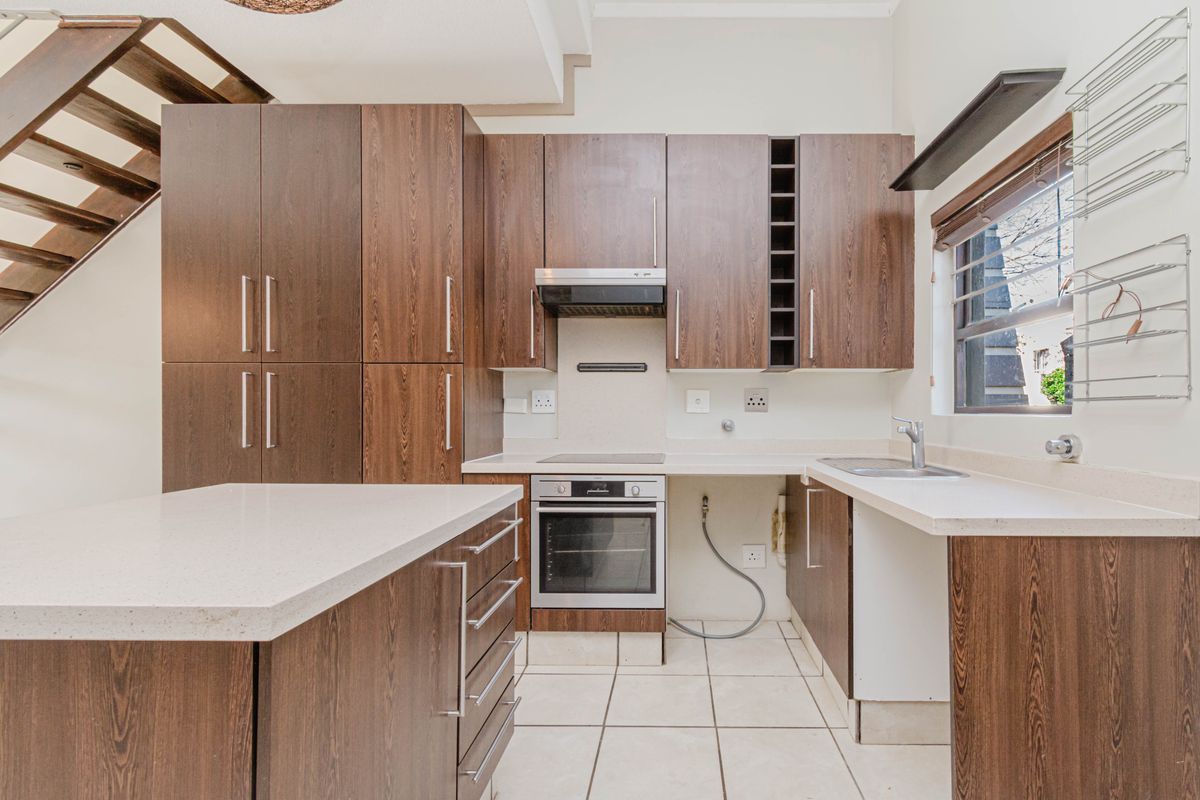 A functional kitchen featuring dark wood cabinetry, stone countertops, built-in oven and hob, and tiled flooring, with an adjacent staircase.
