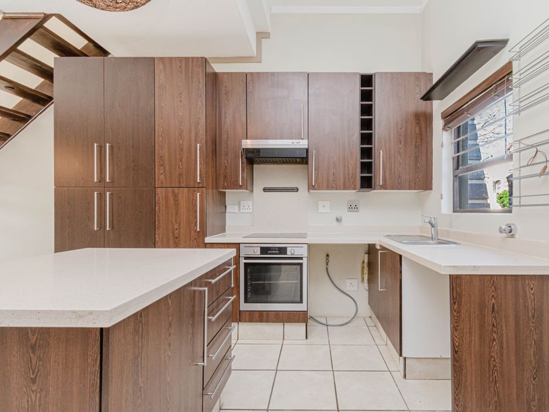 A functional kitchen featuring dark wood cabinetry, stone countertops, built-in oven and hob, and tiled flooring, with an adjacent staircase.
