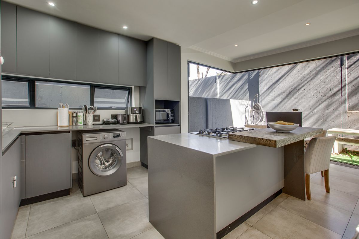 Modern kitchen featuring sleek grey cabinetry, stone countertops, a central island with a gas hob, and integrated laundry facilities with direct outdoor access.