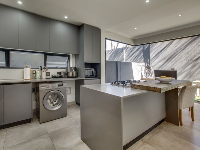 Modern kitchen featuring sleek grey cabinetry, stone countertops, a central island with a gas hob, and integrated laundry facilities with direct outdoor access.