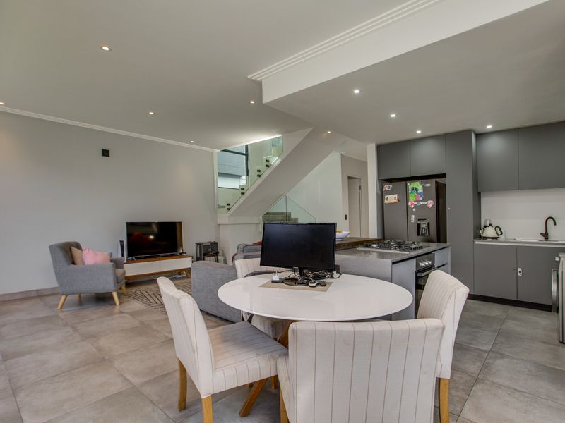 Modern open-plan living area featuring a sleek kitchen with built-in appliances, a central island, and a staircase with a contemporary glass balustrade.