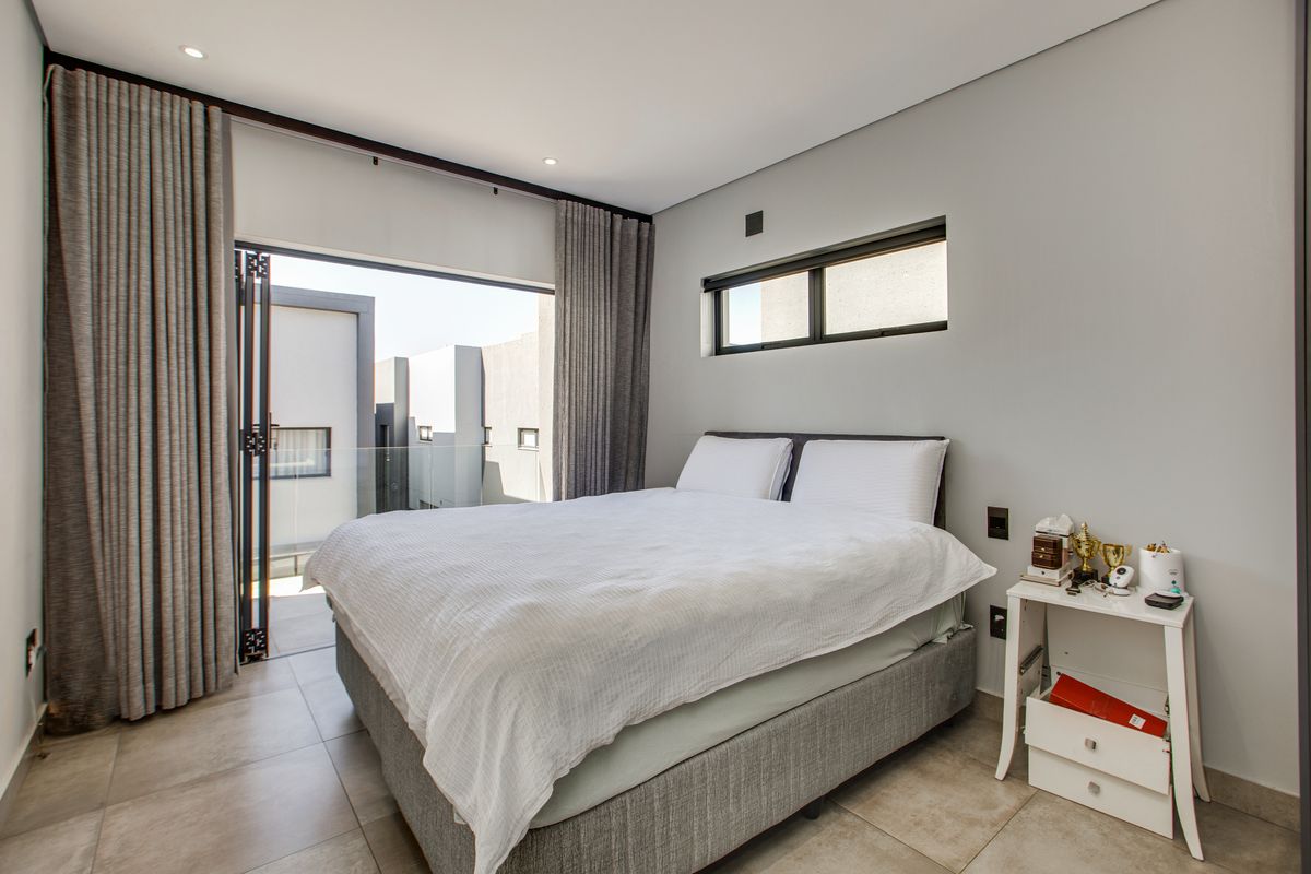 Modern bedroom featuring tiled floors, recessed lighting, and large sliding glass doors opening onto a private balcony with a glass balustrade.