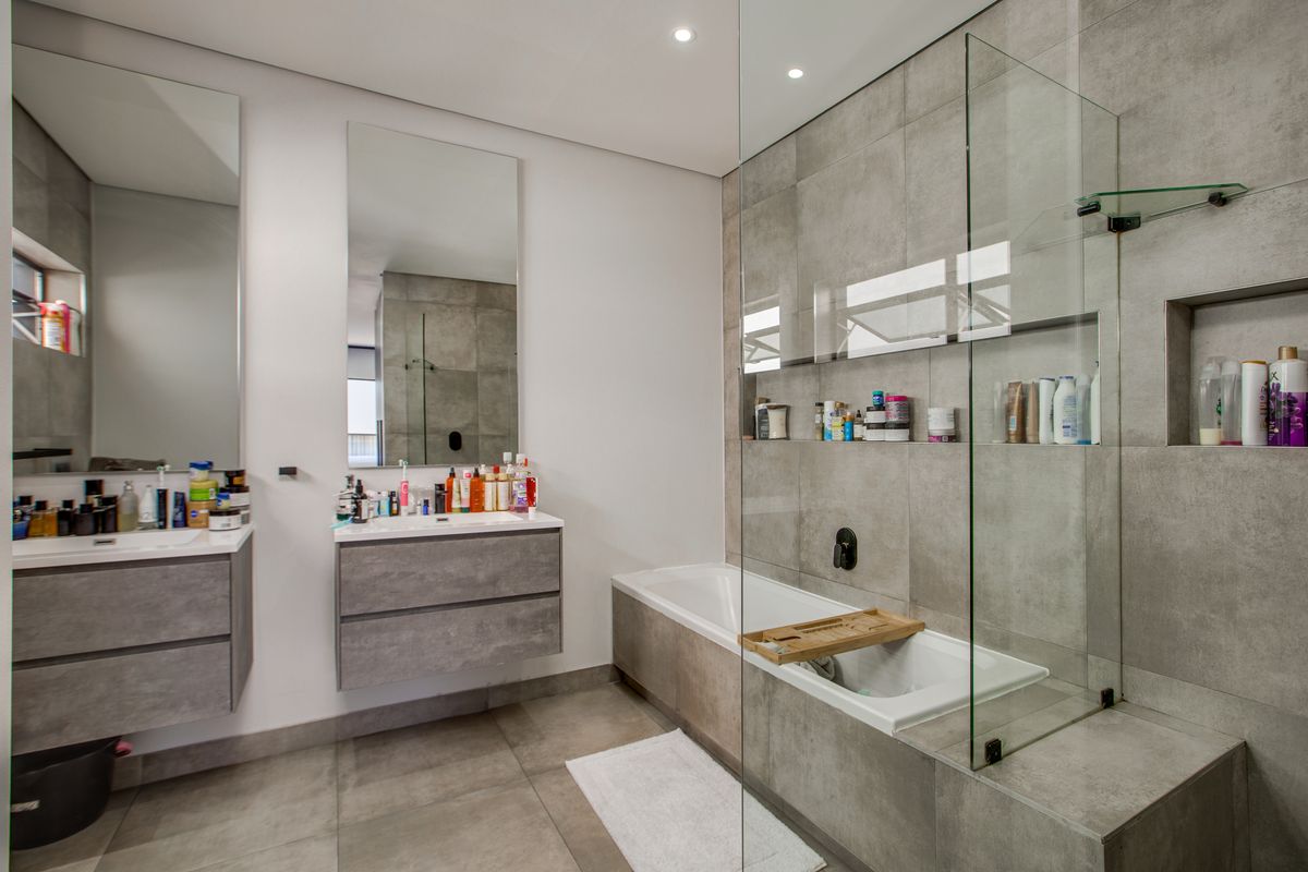 Modern bathroom featuring a floating vanity, built-in bathtub with glass screen, recessed wall niches, and contemporary grey porcelain tiling throughout.