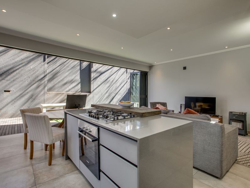 Modern open-plan living area featuring a central kitchen island with gas cooktop, stone countertops, and seamless access to the outdoor patio through large sliding doors.