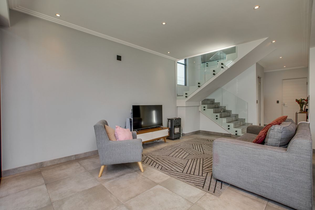 Modern living room featuring tiled flooring, recessed lighting, and a contemporary staircase with a glass balustrade.