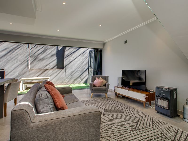 Modern open-plan living area featuring large bi-fold doors that open to an outdoor space, recessed lighting, and sleek tiled flooring.