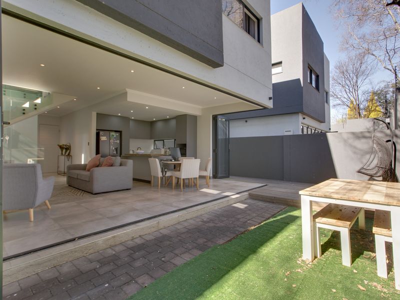 Modern open-plan living area with seamless indoor-outdoor flow through large bi-fold doors to a private patio, garden, and decking area.