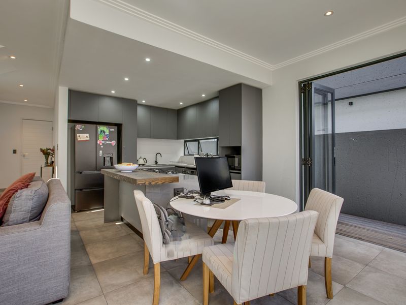 Modern open-plan kitchen and dining area featuring sleek cabinetry, stone countertops, integrated appliances, and bi-fold doors leading to an outdoor space.