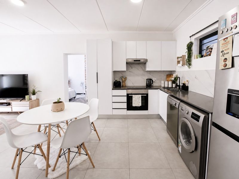 Modern open-plan living area featuring a sleek kitchen with white cabinetry, integrated appliances, marble-look splashback, and neutral tiled flooring throughout.