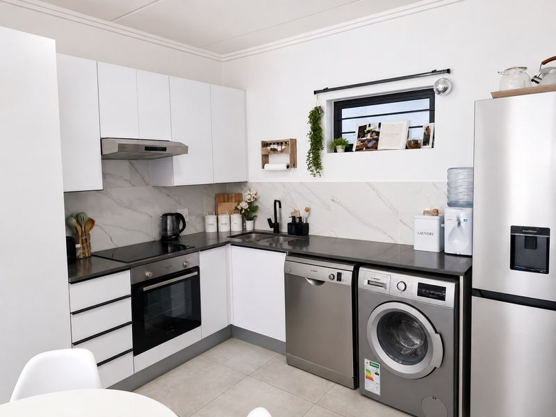 Modern kitchen featuring white cabinetry, marble-look backsplash, dark stone countertops, and integrated appliances including an oven, hob, and extractor fan.