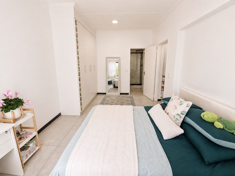 A well-maintained bedroom featuring built-in cupboards, neutral tiled flooring, and direct access to an en-suite bathroom.