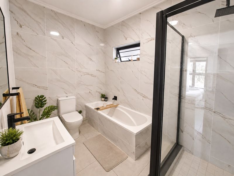 Modern bathroom featuring a walk-in shower with black frame, built-in bathtub, vanity basin, and elegant marble-look wall tiles.