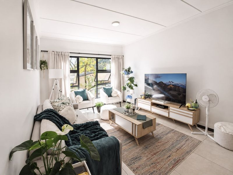 A bright and well-maintained living room featuring neutral tiled flooring and a large window that allows for ample natural light.