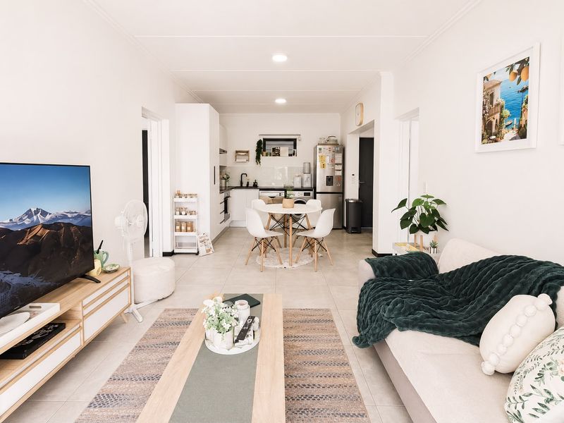 A bright open-plan living and dining area featuring tiled floors, recessed lighting, and a functional kitchen layout with modern cabinetry.